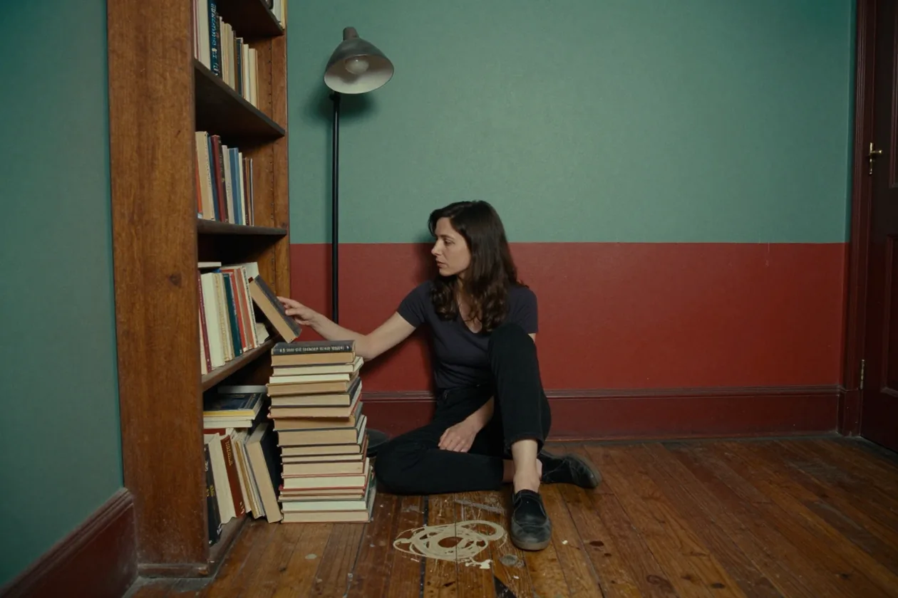 Una donna seduta per terra rimette un libro in uno scaffale basso