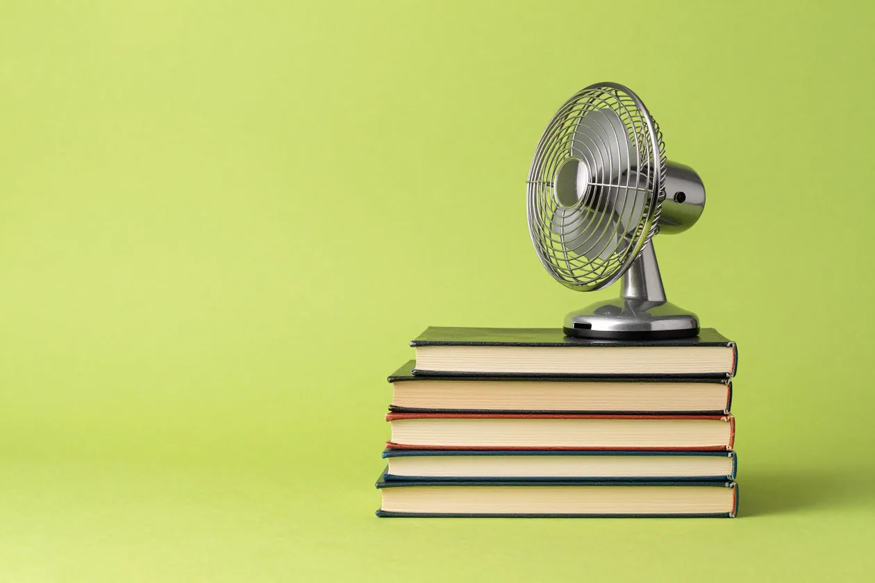 Una pila di libri con un ventilatore da tavolo che ne solleva le pagine