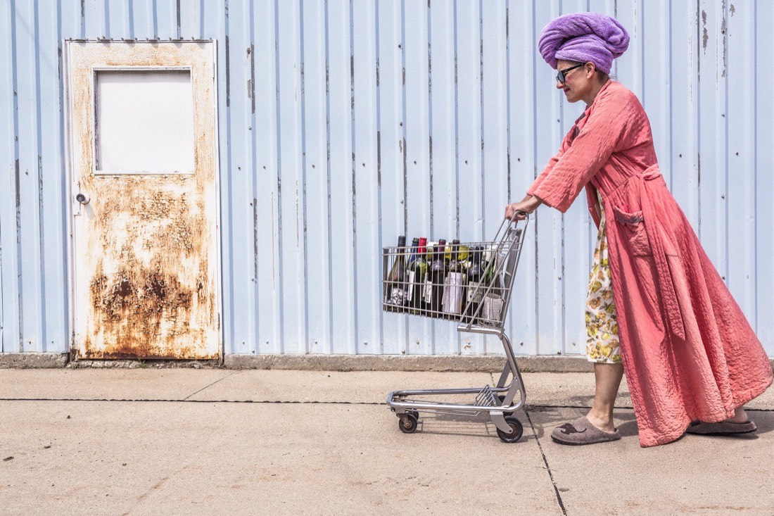 Donna con vestaglia rosa spinge un carrello della spesa lungo un muro azzurro